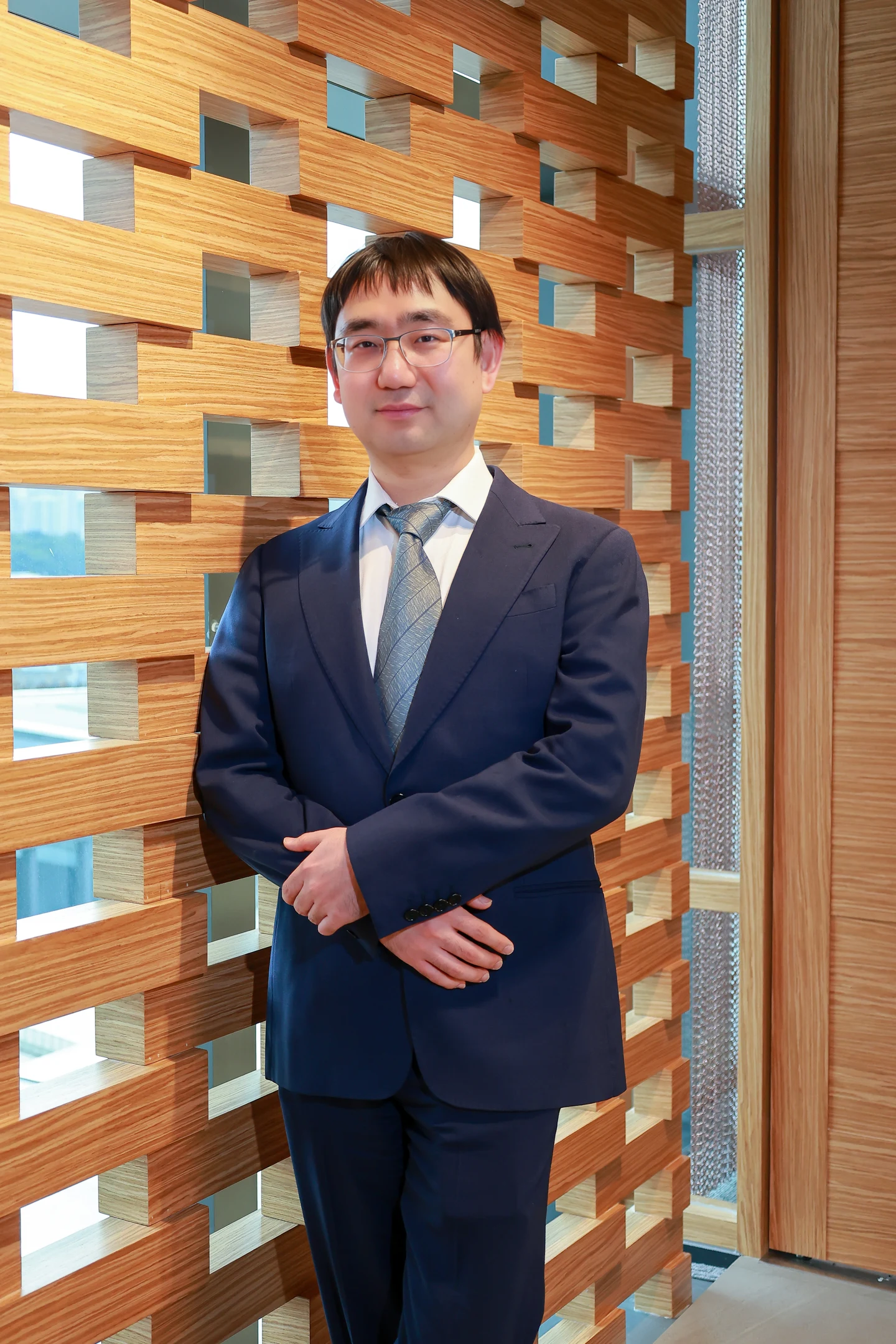Xin Wang standing in front of a wooden screen