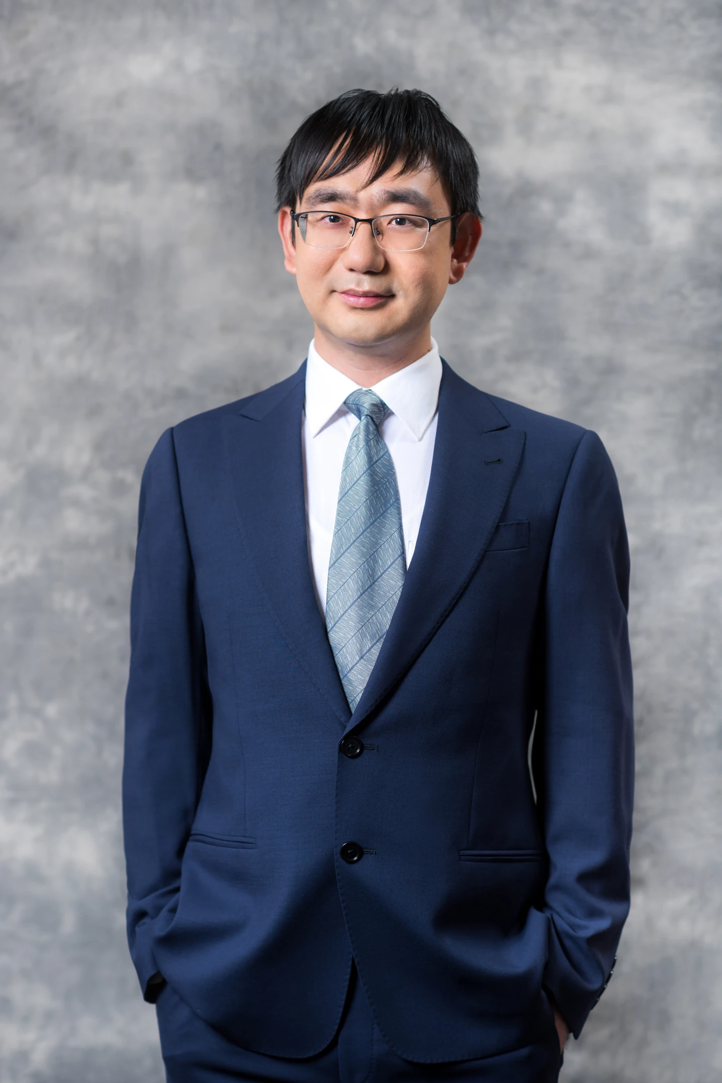 Portrait of Xin Sunny Wang in a navy suit against a grey studio background
